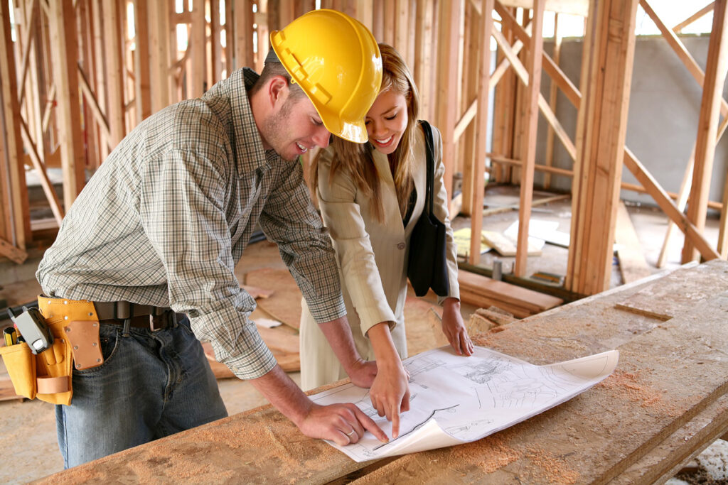 A home builder in a yellow hard hat reviewing home blueprints with a client in El Paso.
